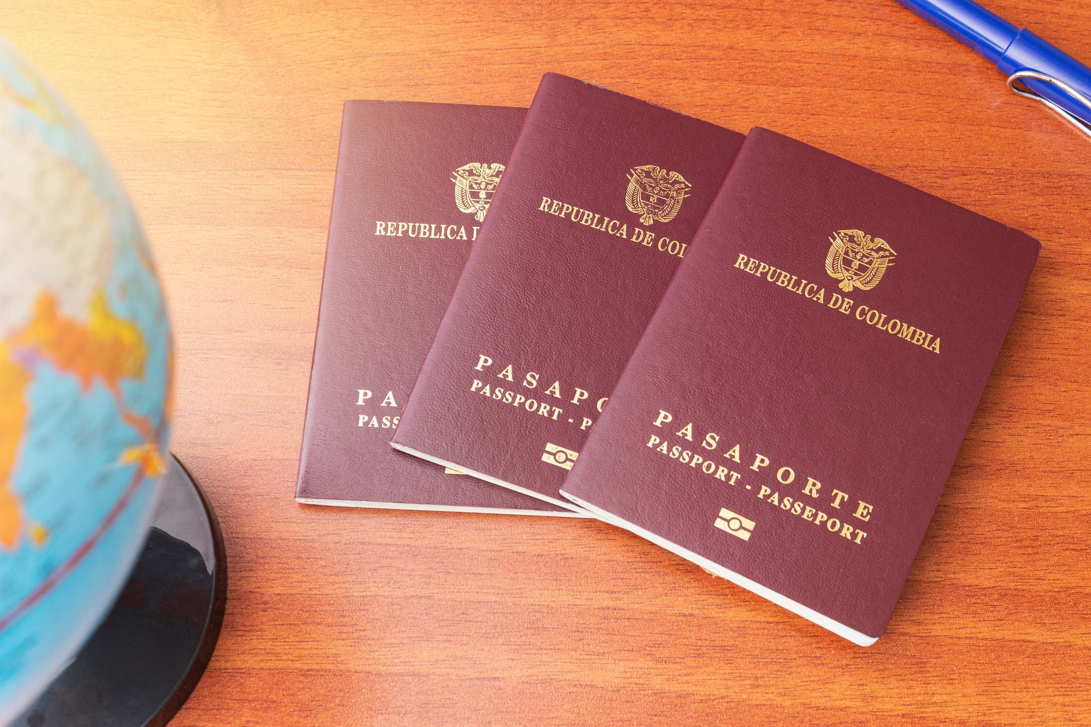 Three Colombian passports fanned out next to a globe and a pen on a wooden desk